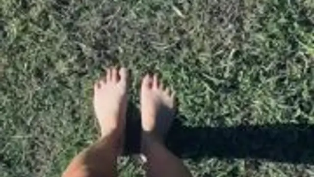 Gebräunte nackte Füße, die langsam über grünes Gras laufen.